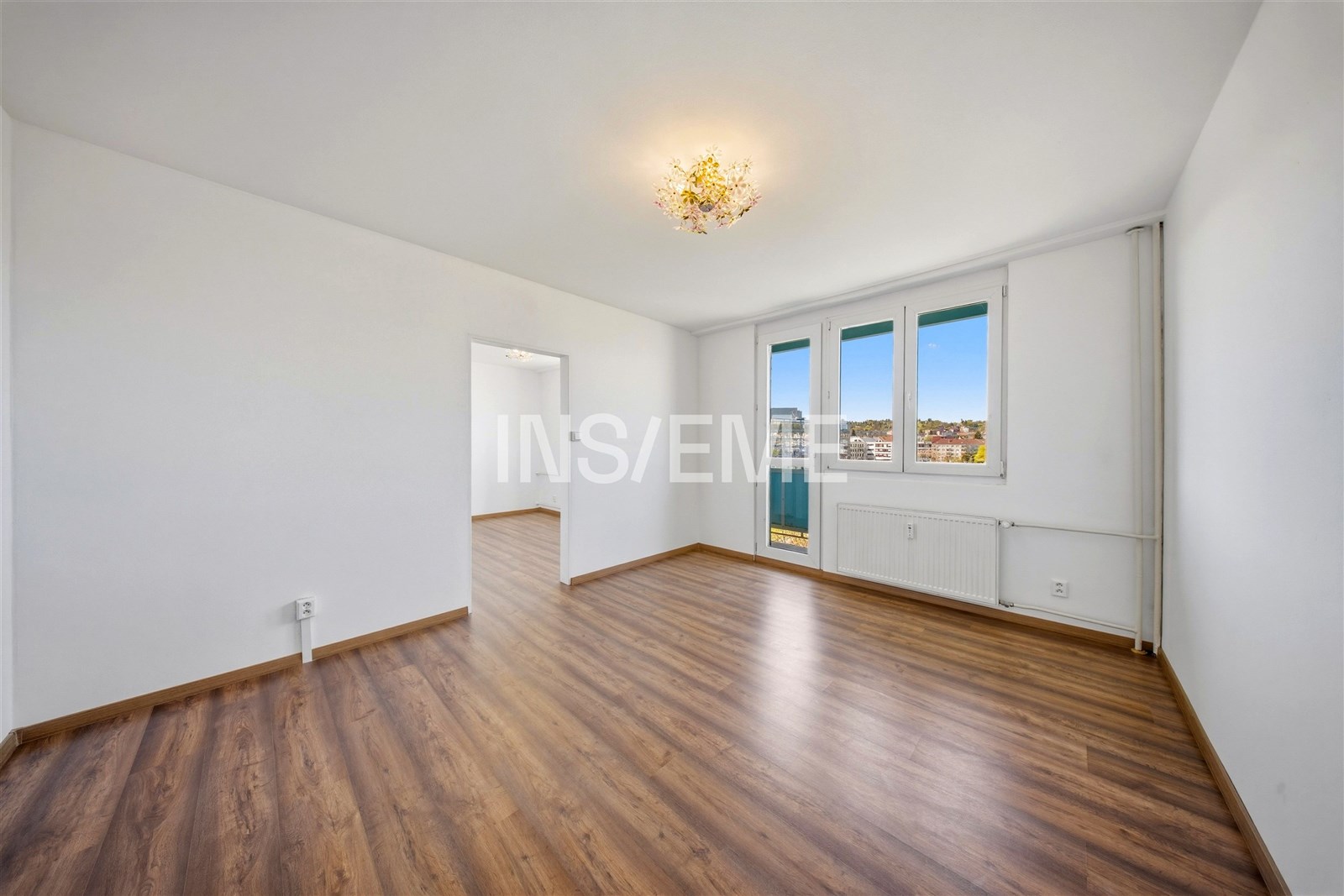 Světlý obývací pokoj s parketovou podlahou, velká okna, moderní styl, výhled na město, vhodný pro rodinné bydlení.