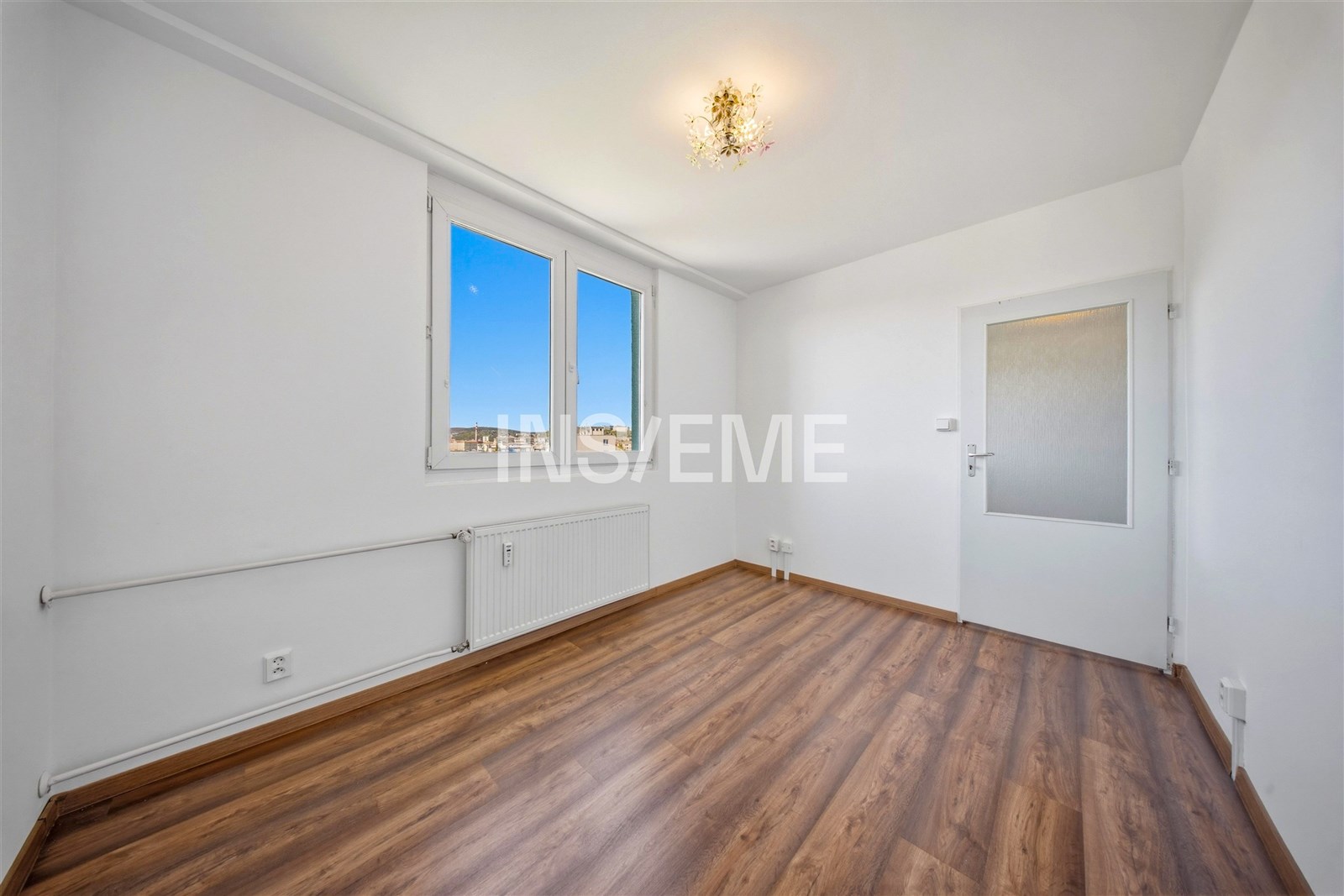 Světlá ložnice s laminátovou podlahou, velká okna poskytují výhled a moderní osvětlení dodává elegantní styl.