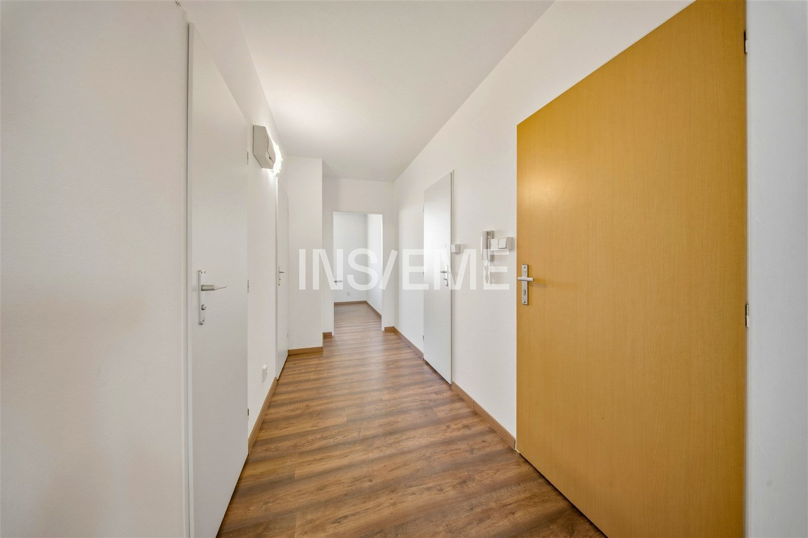 Úzká chodba s laminátovou podlahou, bílými stěnami a moderními dveřmi, poskytuje přístup ke světlým pokojům ve zrekonstruovaném bytě.